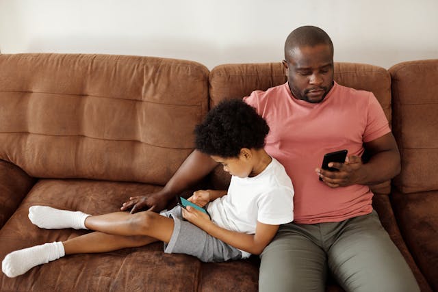 A man sitting on a sofa with this son. They are both using smartphones (Photo: August de Richelieu)